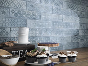 Decorative tile pattern on a wall with a table displaying cupcakes and tea items.